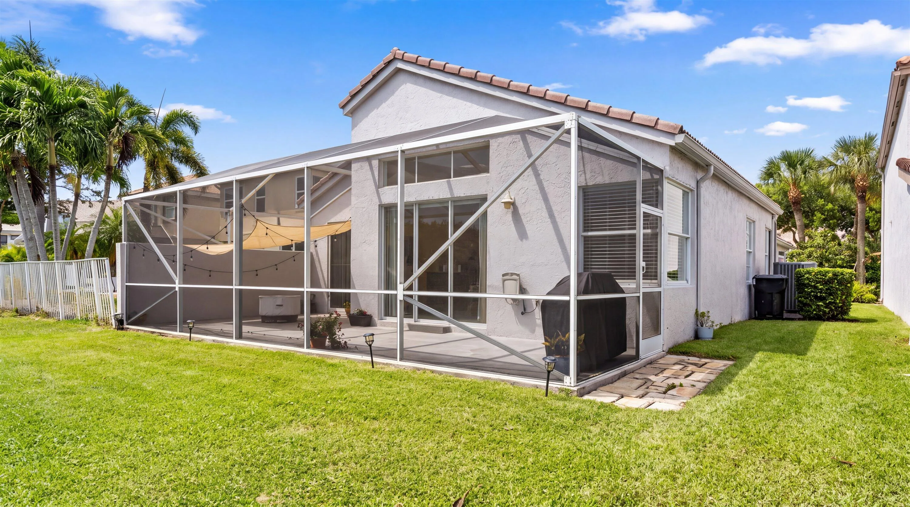 Expansive screened-in patio with tiled flooring and a stucco exterior, surrounded by a manicured lawn and mature palm trees