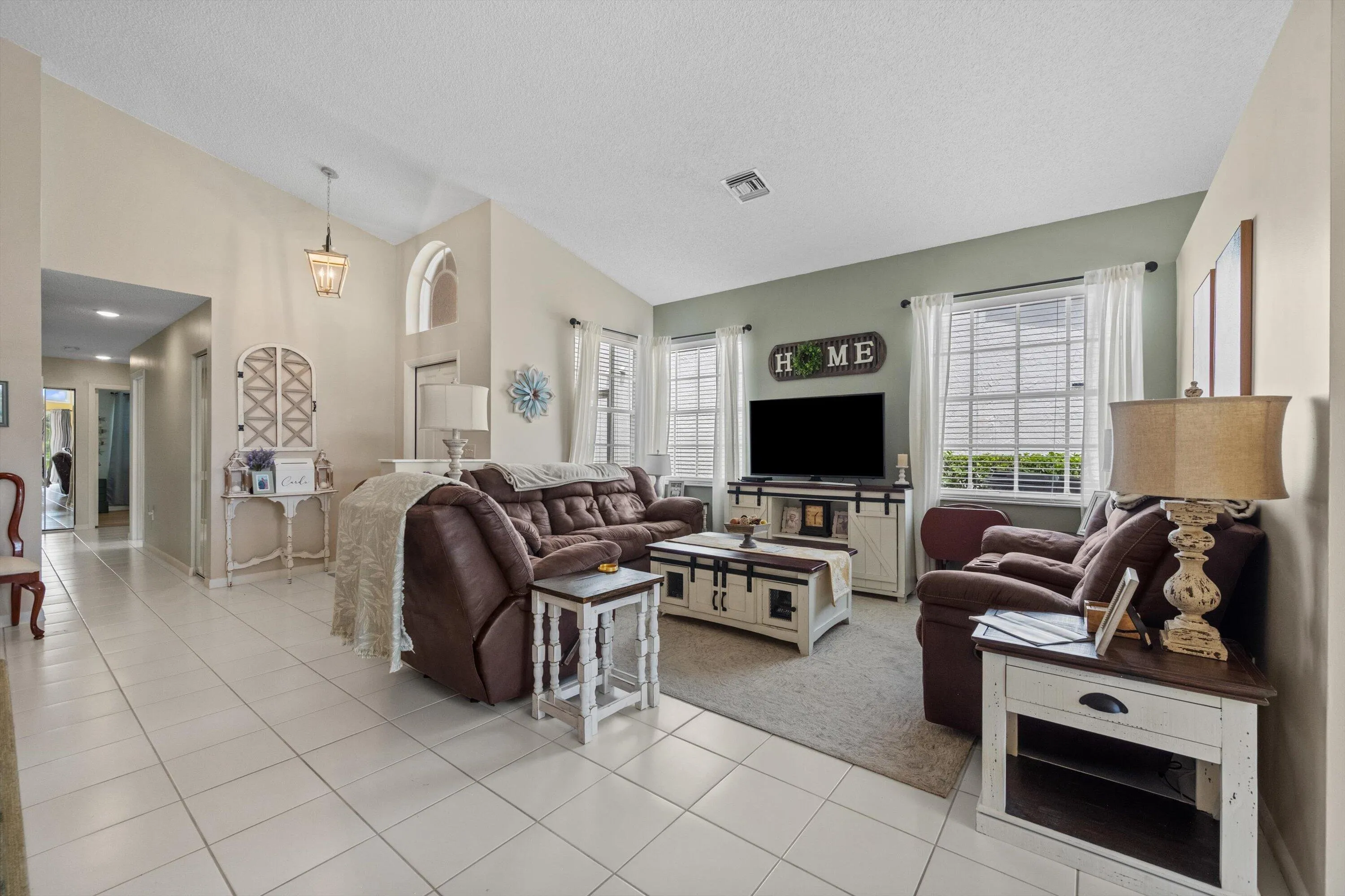 Vaulted ceiling with pendant lighting, tile flooring, and multiple windows with blinds