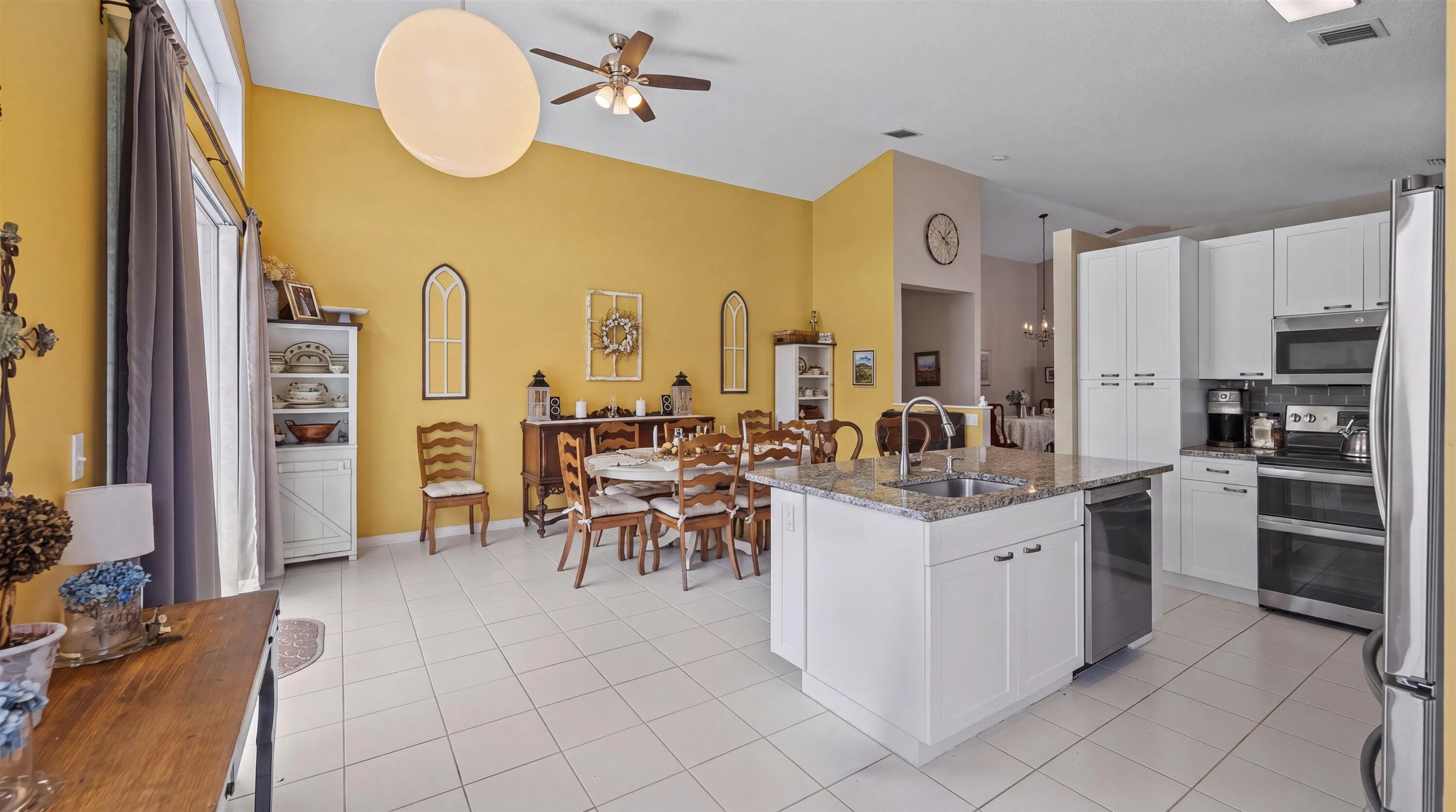 Kitchen island with granite countertop and double sink, white cabinetry with integrated appliances, and light-toned tile flooring