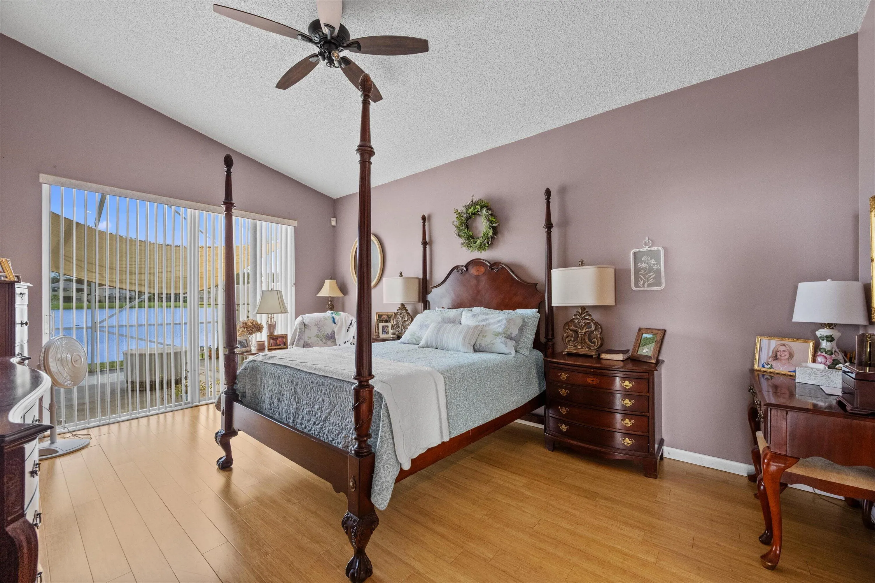 Vaulted ceiling with a ceiling fan, light wood-finish flooring, sliding glass door, vertical blinds, and water scenery
