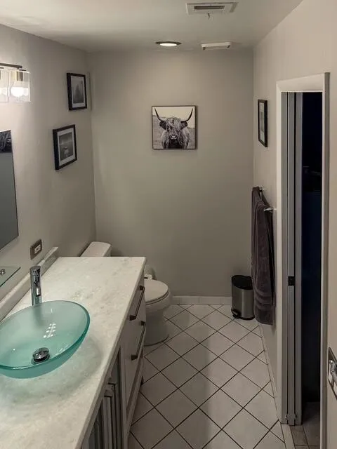 White tile flooring with dark grout, light-colored vanity with a vessel sink, wall-mounted lighting fixture, and recessed ceiling lights