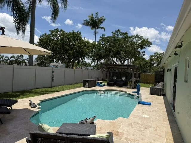 Backyard oasis featuring a swimming pool, travertine-style patio, and a privacy fence