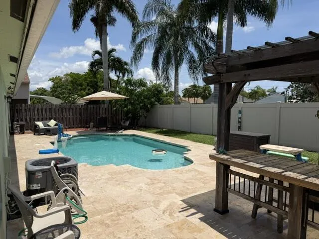 Outdoor living area featuring a swimming pool, wood pergola, and travertine-style paver patio