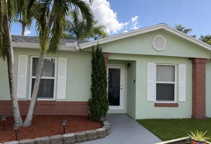 Stucco exterior with brick detailing, white window shutters, gabled roofline, and front entry with glass panel door
