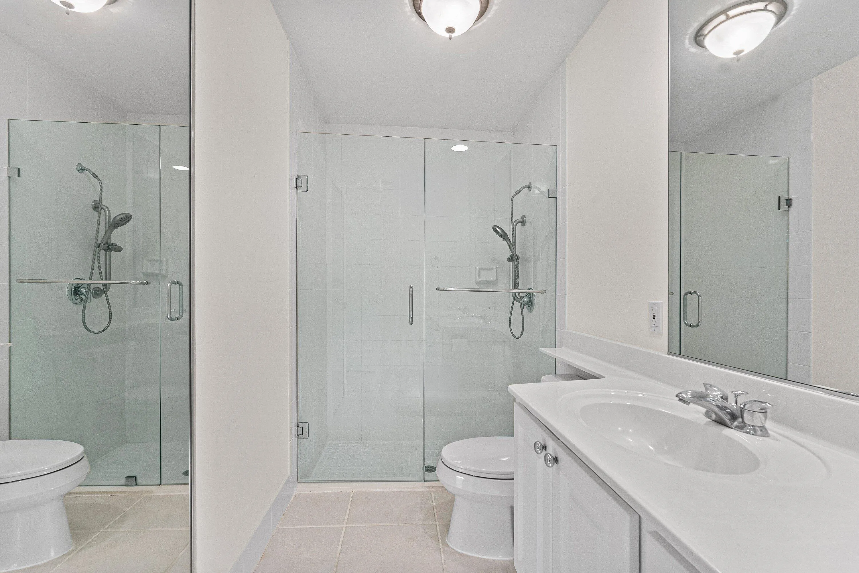 Glass-enclosed shower, white vanity with integrated sink, chrome faucet, wall-mounted mirror, and recessed lighting
