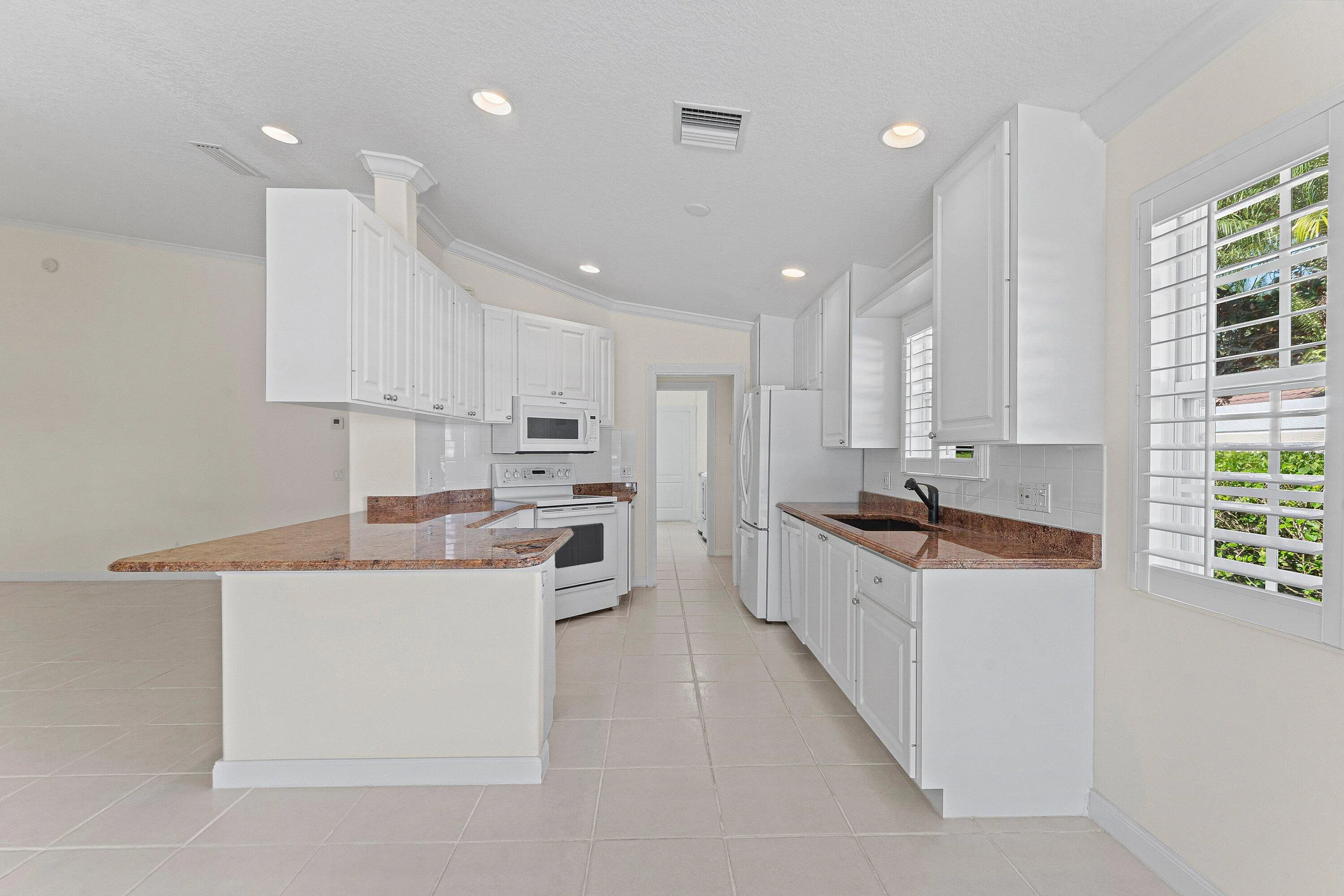 Kitchen featuring white cabinetry, granite countertops, white tile flooring, white appliances, and plantation shutters