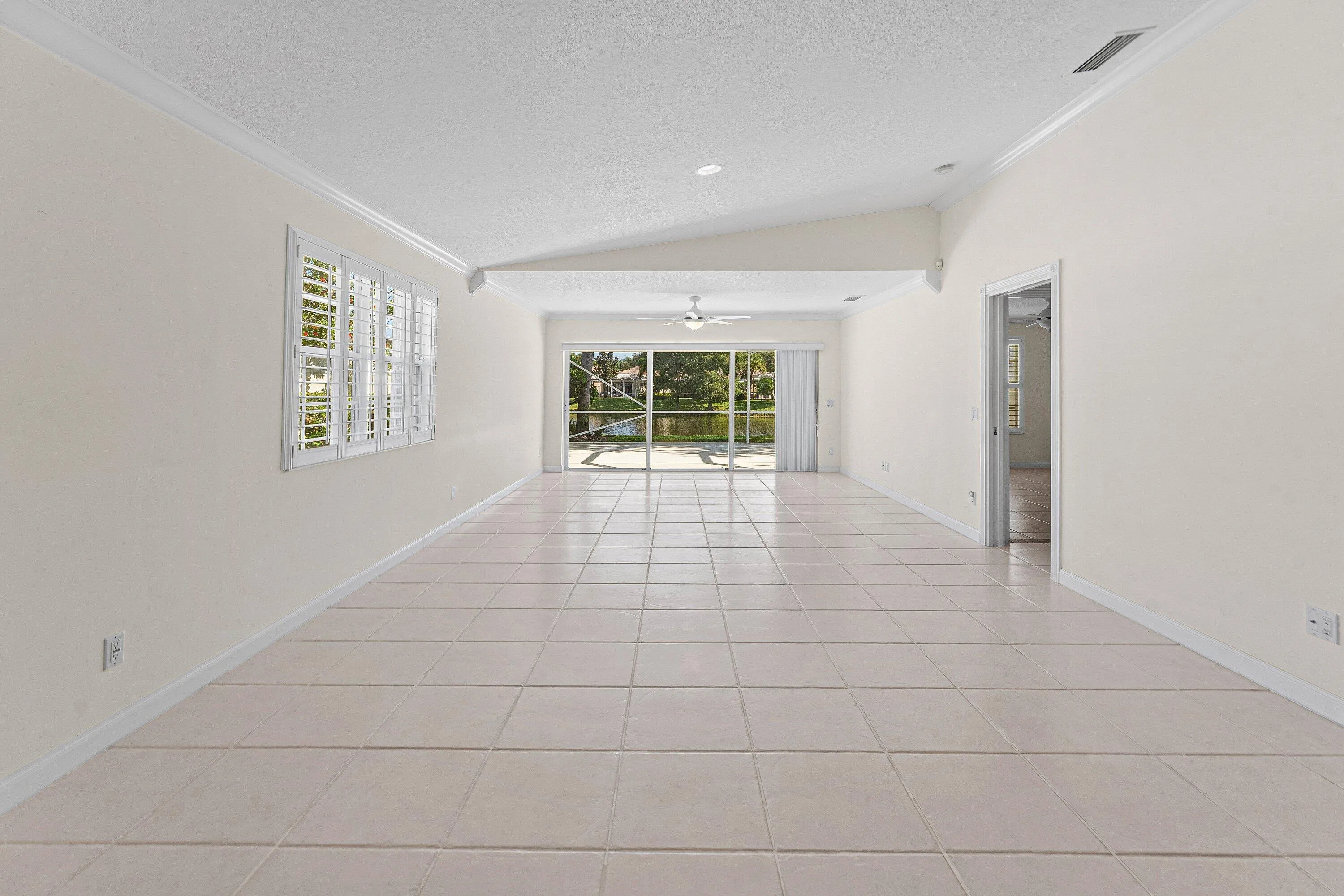 Spacious interior with tile flooring, plantation shutters, vaulted ceiling, and sliding glass doors