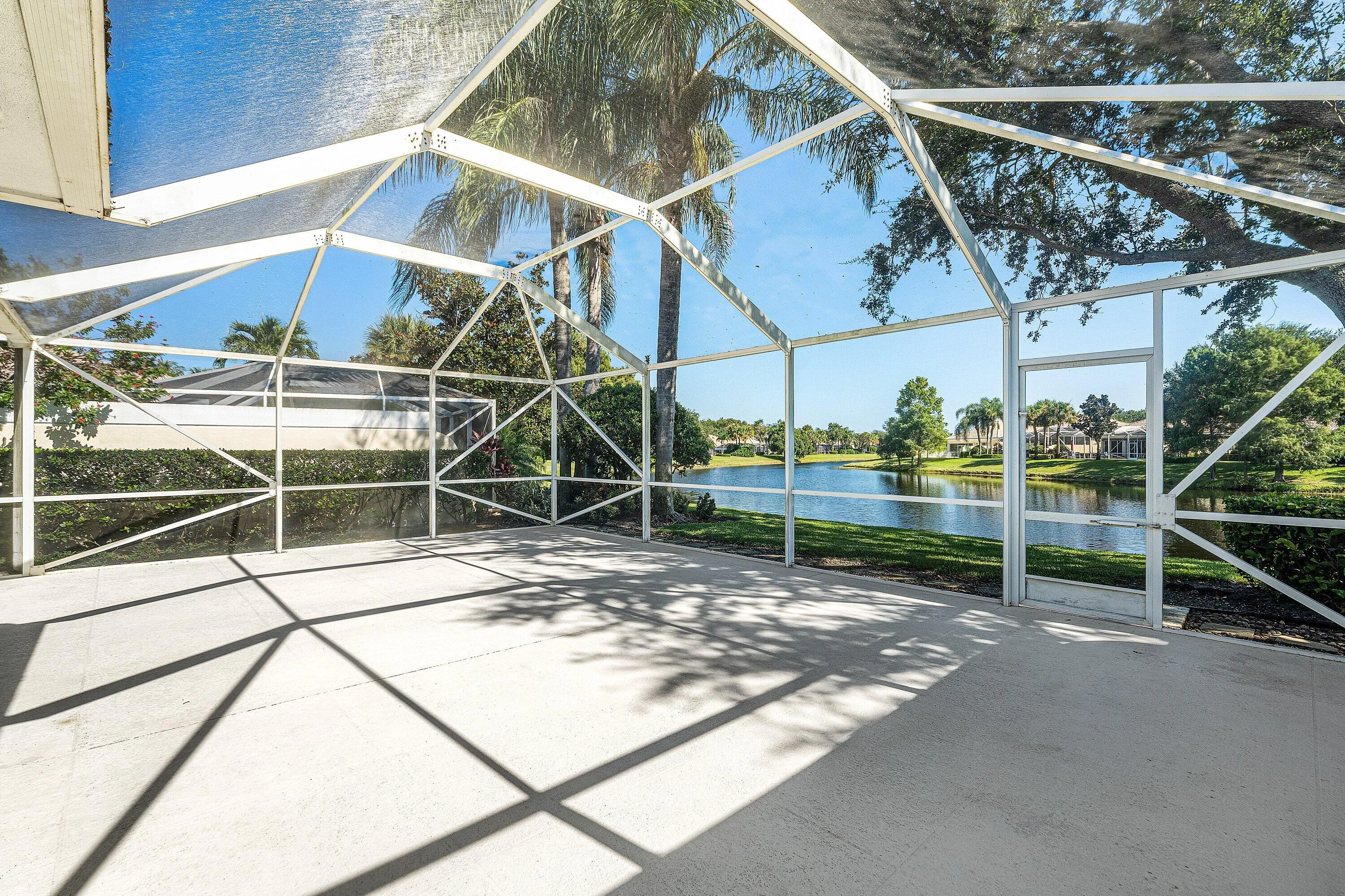 Expansive screened patio featuring a concrete surface, direct access to a waterfront, and surrounding mature landscaping
