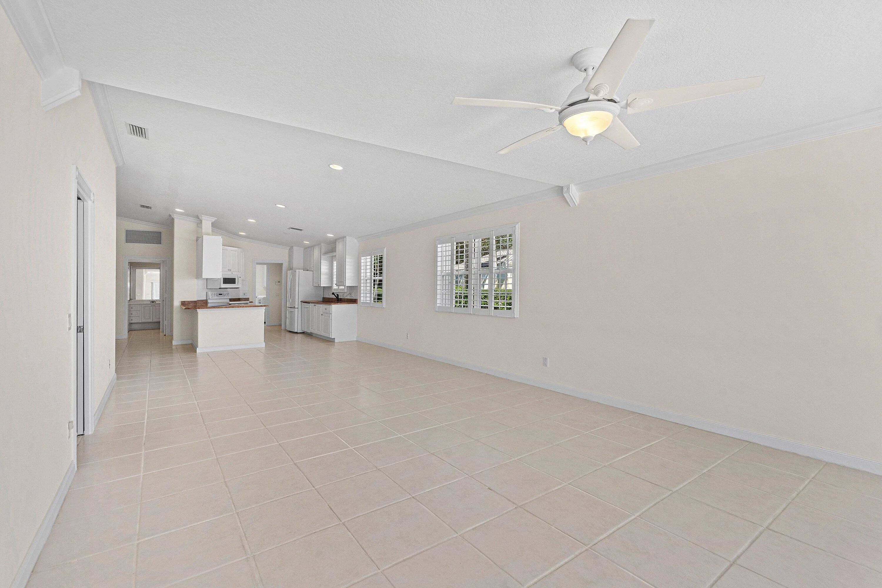 Spacious room featuring tile flooring, vaulted ceilings, a ceiling fan with integrated lighting, and multiple windows with plantation shutters