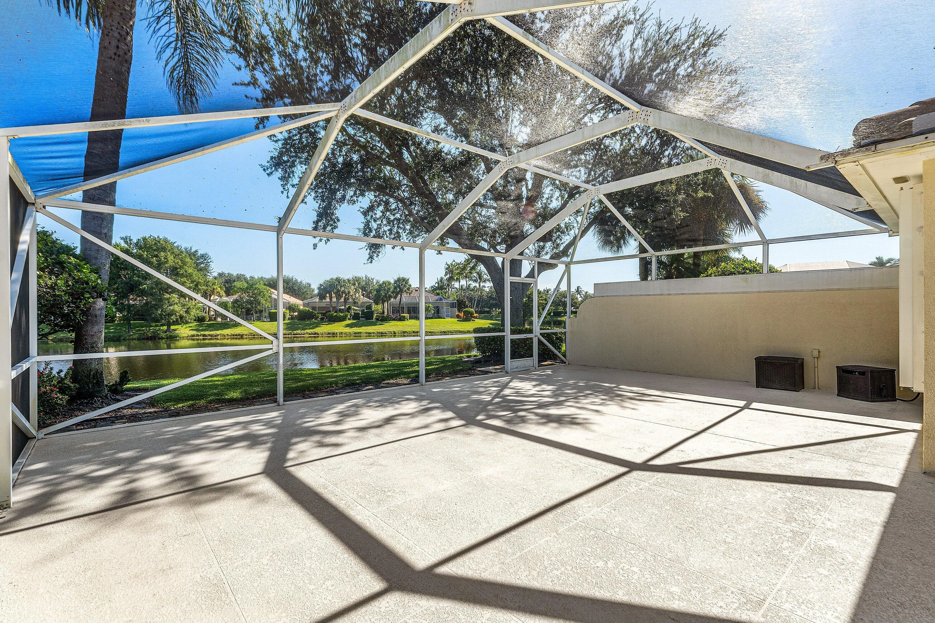 Screened outdoor living space featuring a concrete patio, lakefront setting, and mature foliage