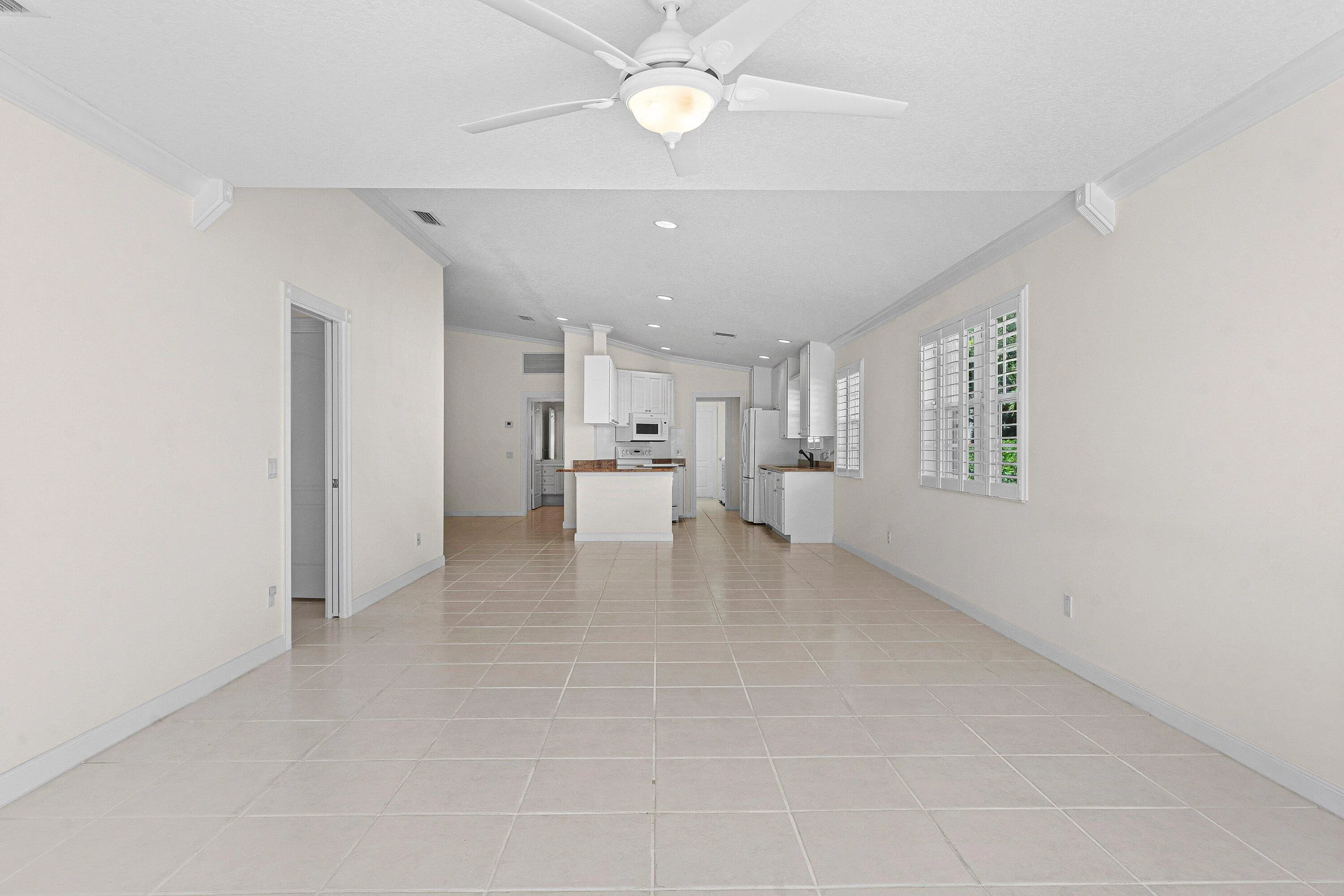 Spacious room with light-toned tile flooring, white walls, and a ceiling fan