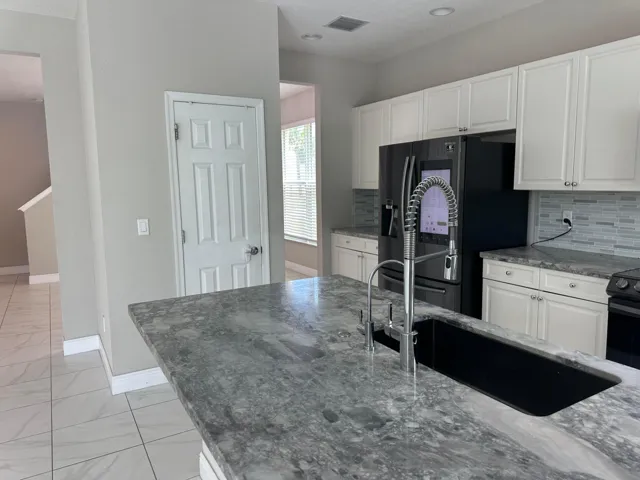 Kitchen before staging. Glass tiled backsplash, stone countertops, smart fridge, pantry, wood cabinetry