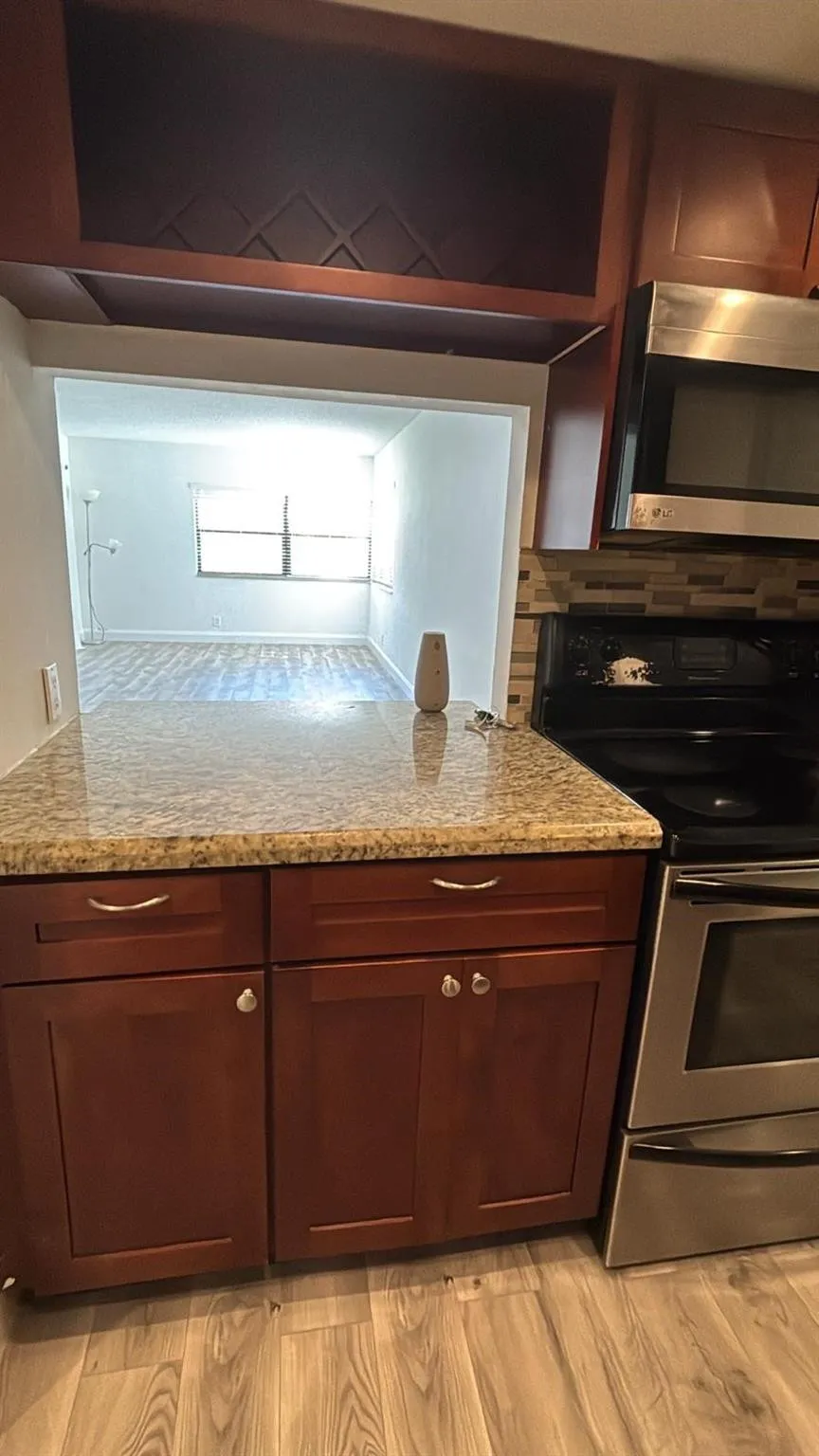Kitchen featuring wood-finish cabinetry, granite-style countertops, stainless steel appliances, and a mosaic tile backsplash
