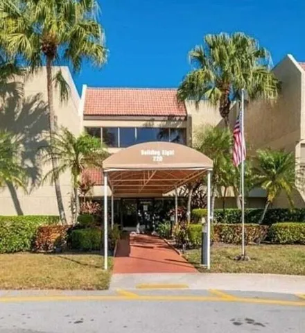 Building exterior with a terracotta-tiled roof, multiple large windows, a covered entryway, and surrounding mature palm trees