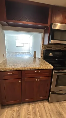Kitchen featuring wood-finish cabinetry, granite-style countertops, stainless steel appliances, and a mosaic tile backsplash