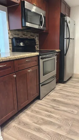 Kitchen featuring wood-finish cabinetry, stone-look countertops, stainless steel appliances, and a mosaic tile backsplash
