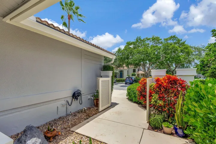Exterior pathway featuring diverse landscaping with colorful foliage, a stucco exterior, and a tiled roofline