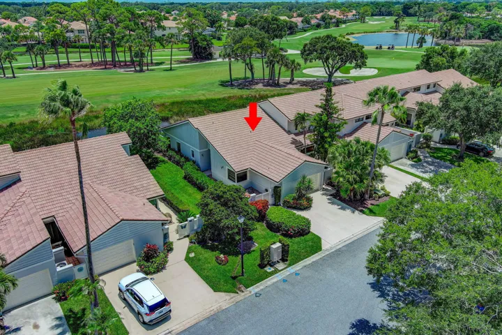 Tile roof, attached garage, paved driveway, mature landscaping, and a golf course setting