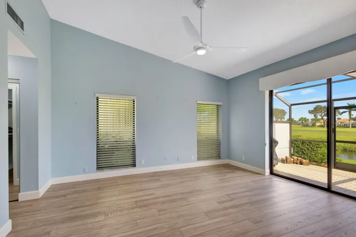 Another view of the primary bedroom highlights two additional windows that fill the room with natural light, along with wood-look laminate flooring and beautiful views of the Champion Course.