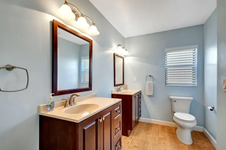 Bright primary bathroom with two separate vanities, a private toilet area, and a window that brings in natural light.