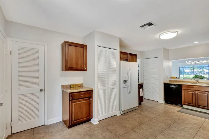 Kitchen featuring tile flooring, wood cabinetry, stone-finish countertops, black dishwasher, and white refrigerator