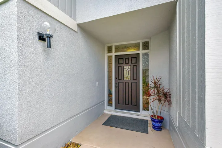 Recessed entry with textured stucco siding, panel door with decorative glass inserts, and transom windows