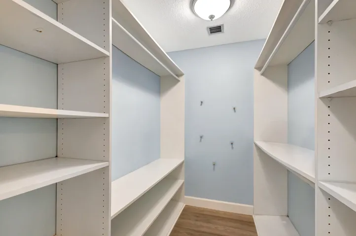 Spacious primary walk-in closet featuring custom white wood shelving for organized and convenient storage.
