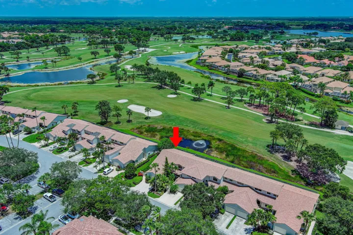 Aerial view of this golf course community property featuring manicured grounds, mature landscaping with palm trees, and direct access to the championship fairway and water features