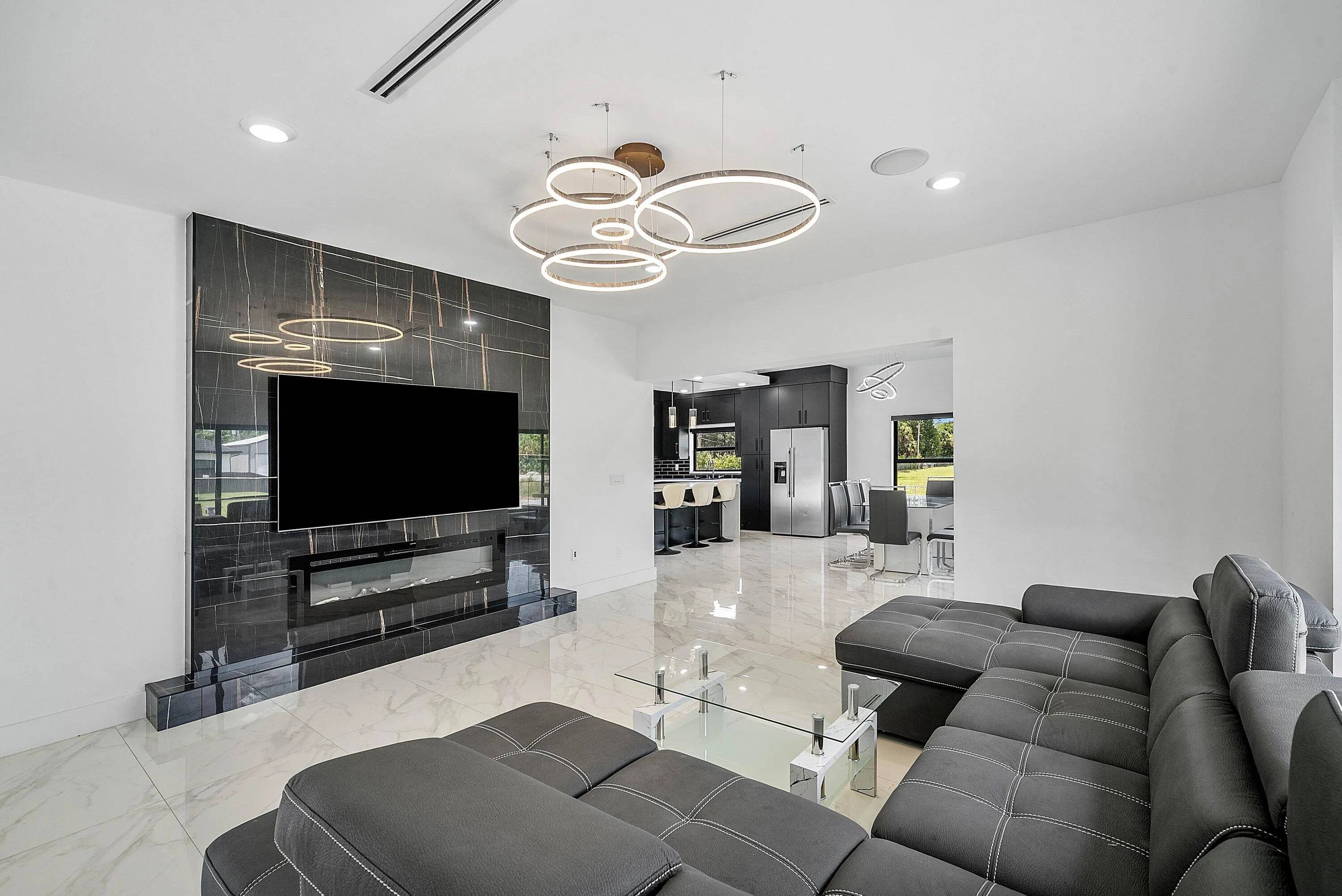 Porcelain tile flooring, built-in electric fireplace, wall-mounted television, recessed lighting, and contemporary circular chandelier