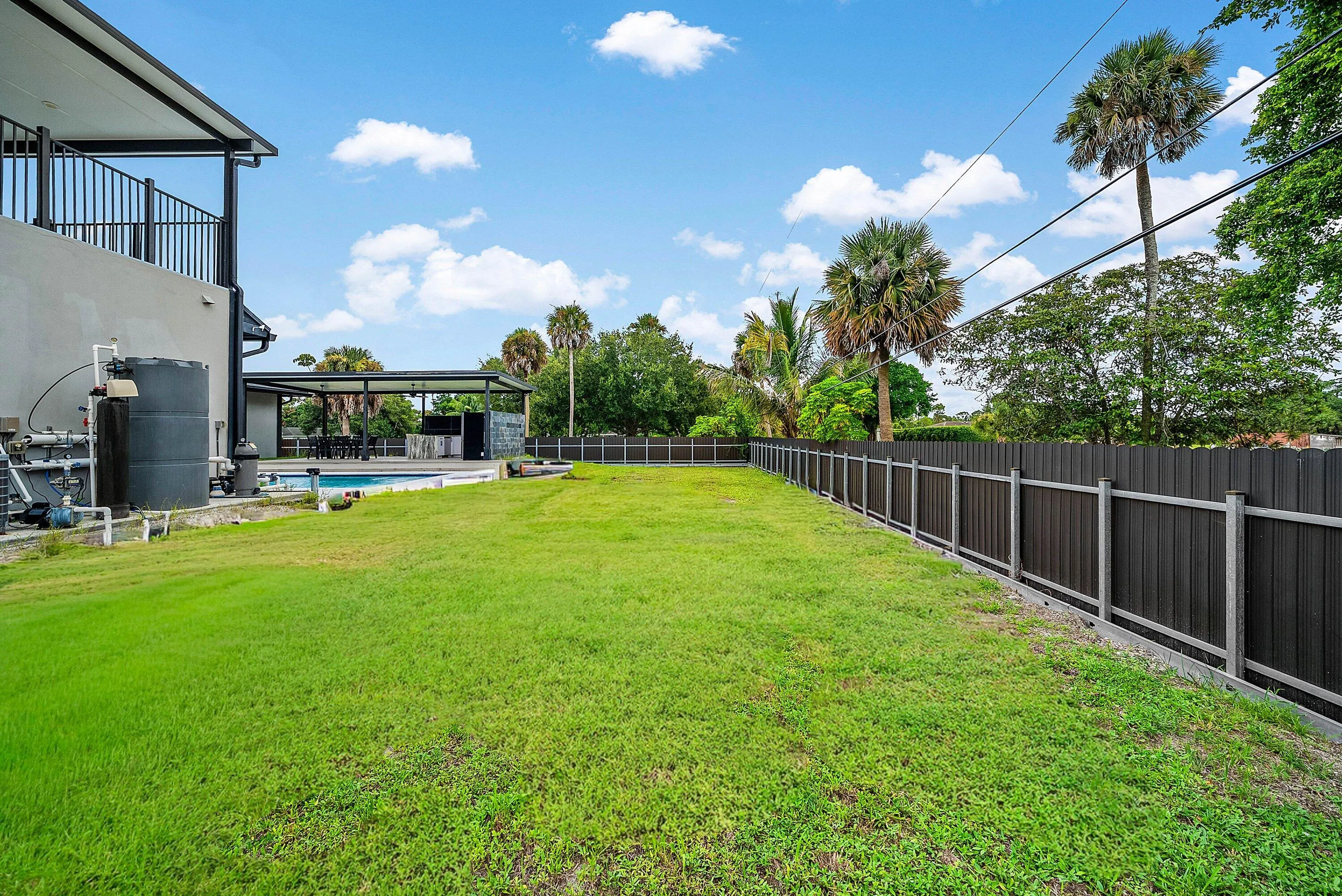 Expansive grass area with a dark panel fence, bordering a covered outdoor entertainment space and pool