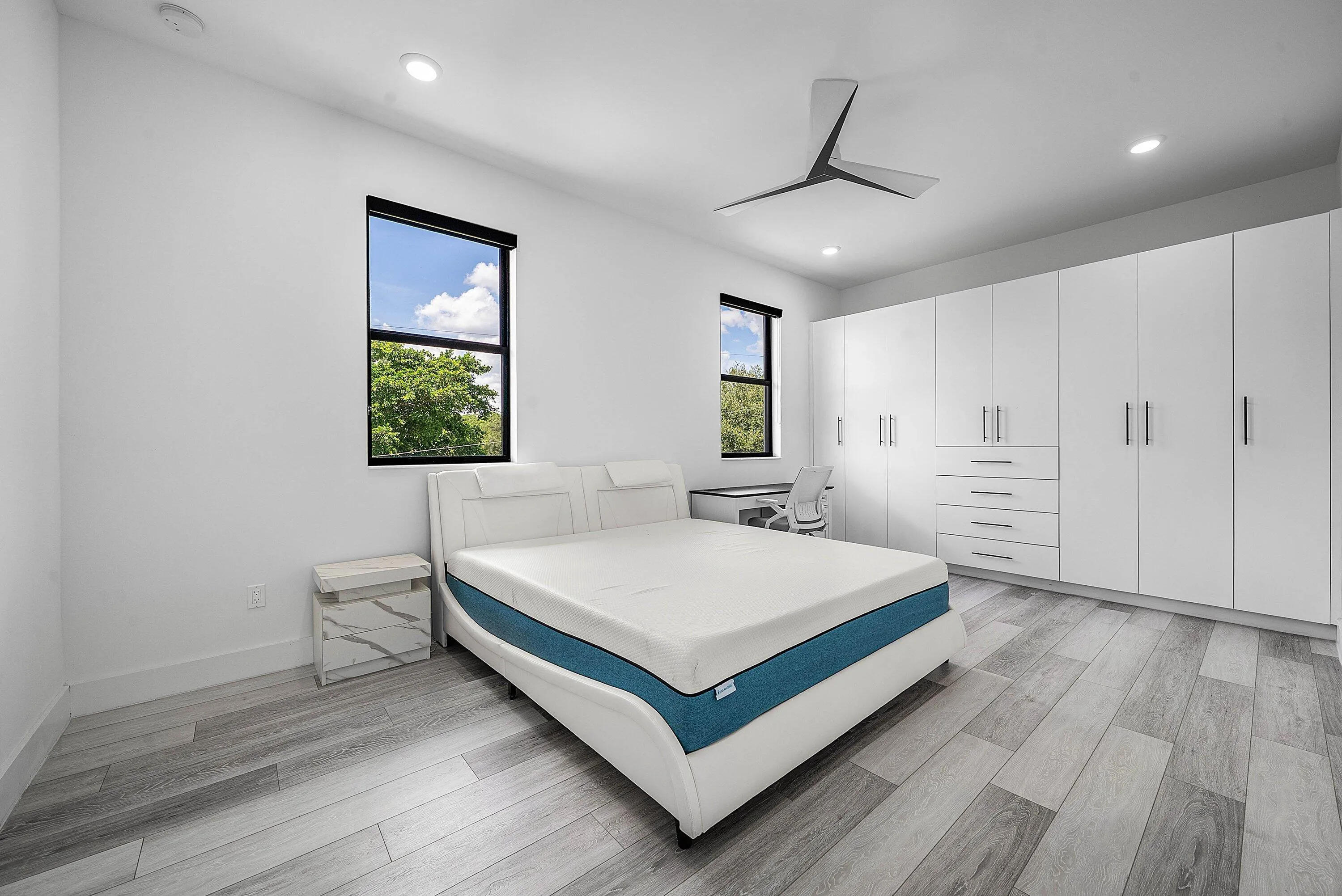 Expansive built-in wardrobe system with ample storage, contemporary ceiling fan, recessed lighting, wood-finish flooring, and multiple windows