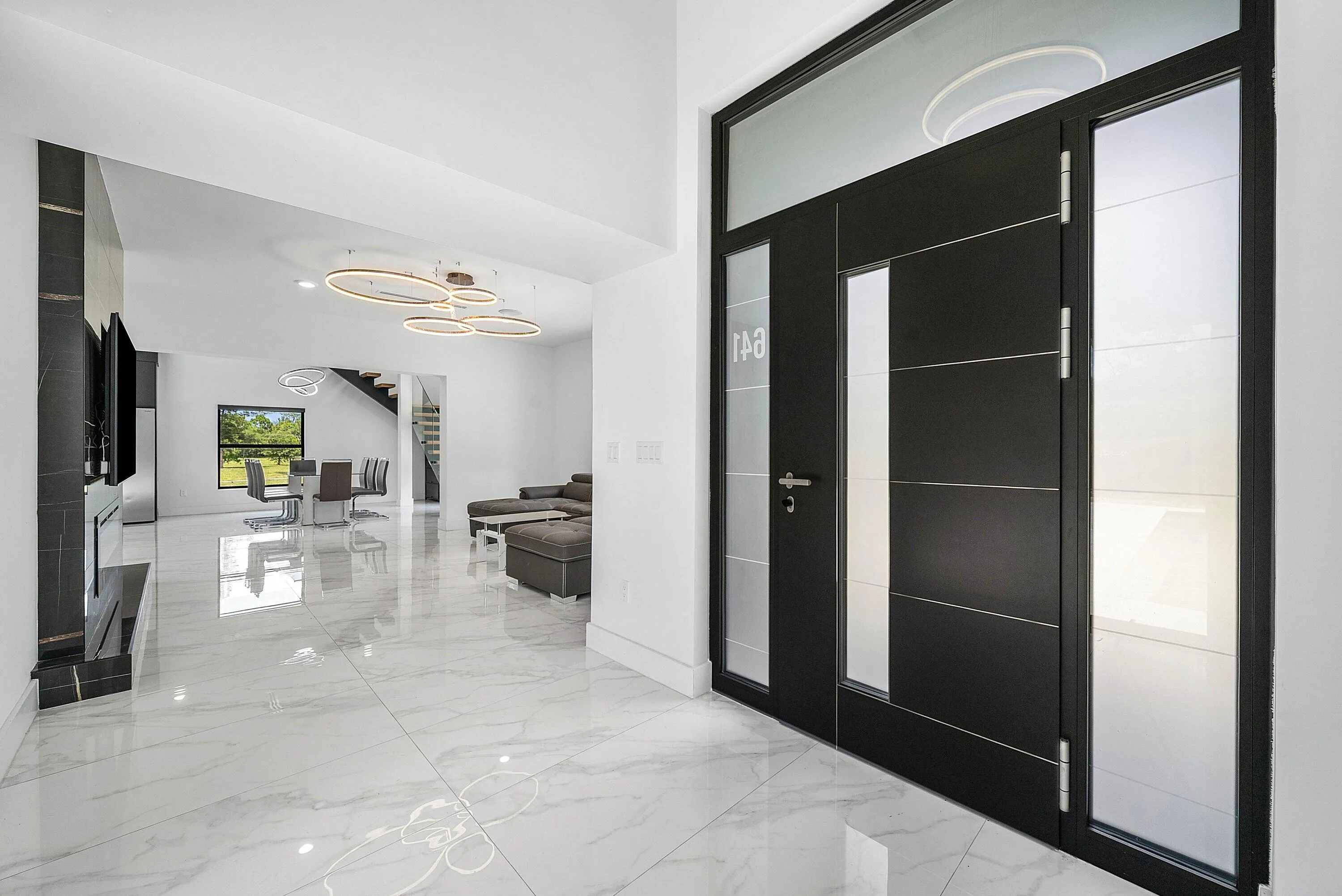 Modern entry door with frosted glass panels, white marble-look flooring, built-in media console, and a contemporary ceiling light fixture