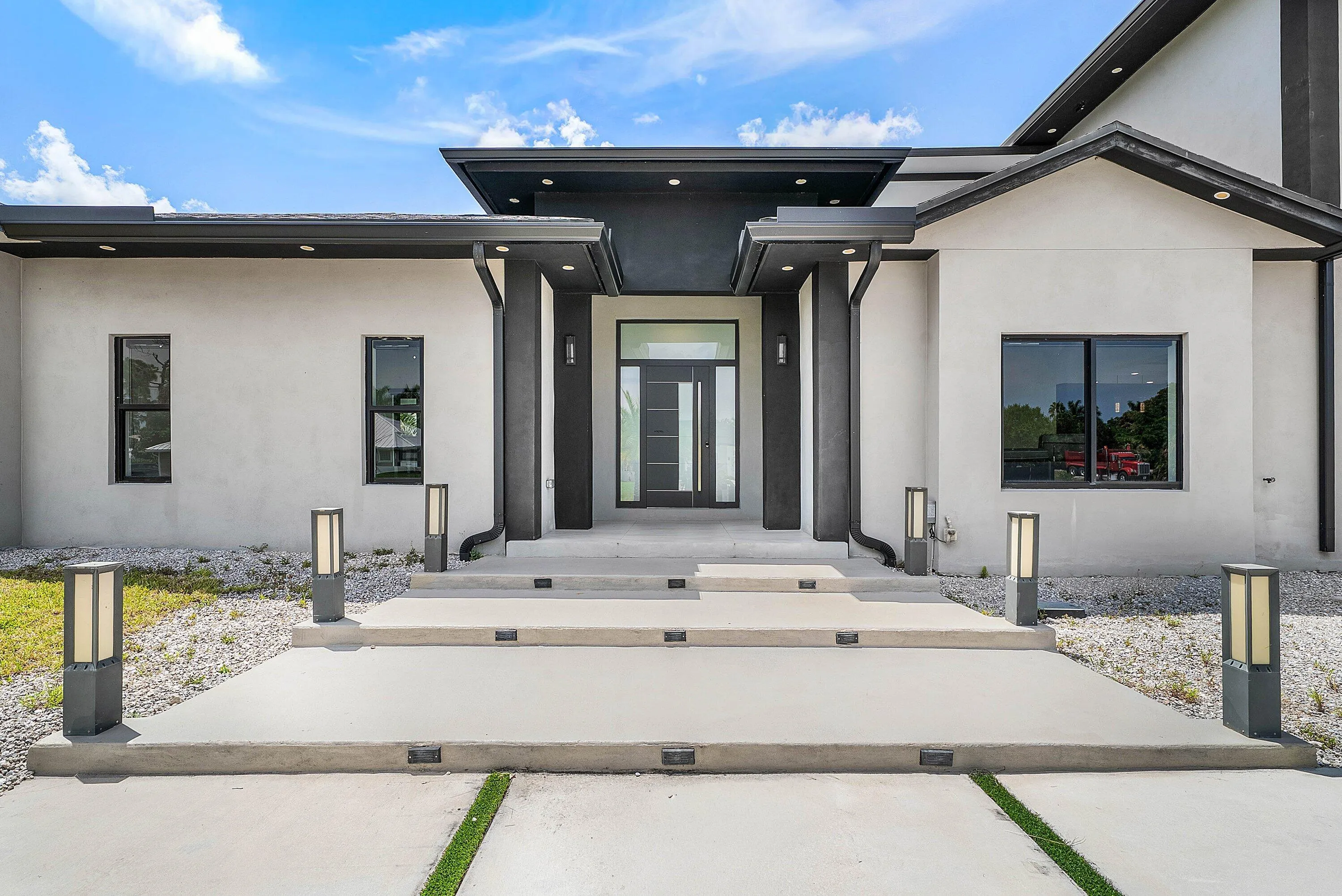 Modern stucco exterior featuring a tiered concrete entry, a dark-framed glass paneled front door, and integrated outdoor lighting
