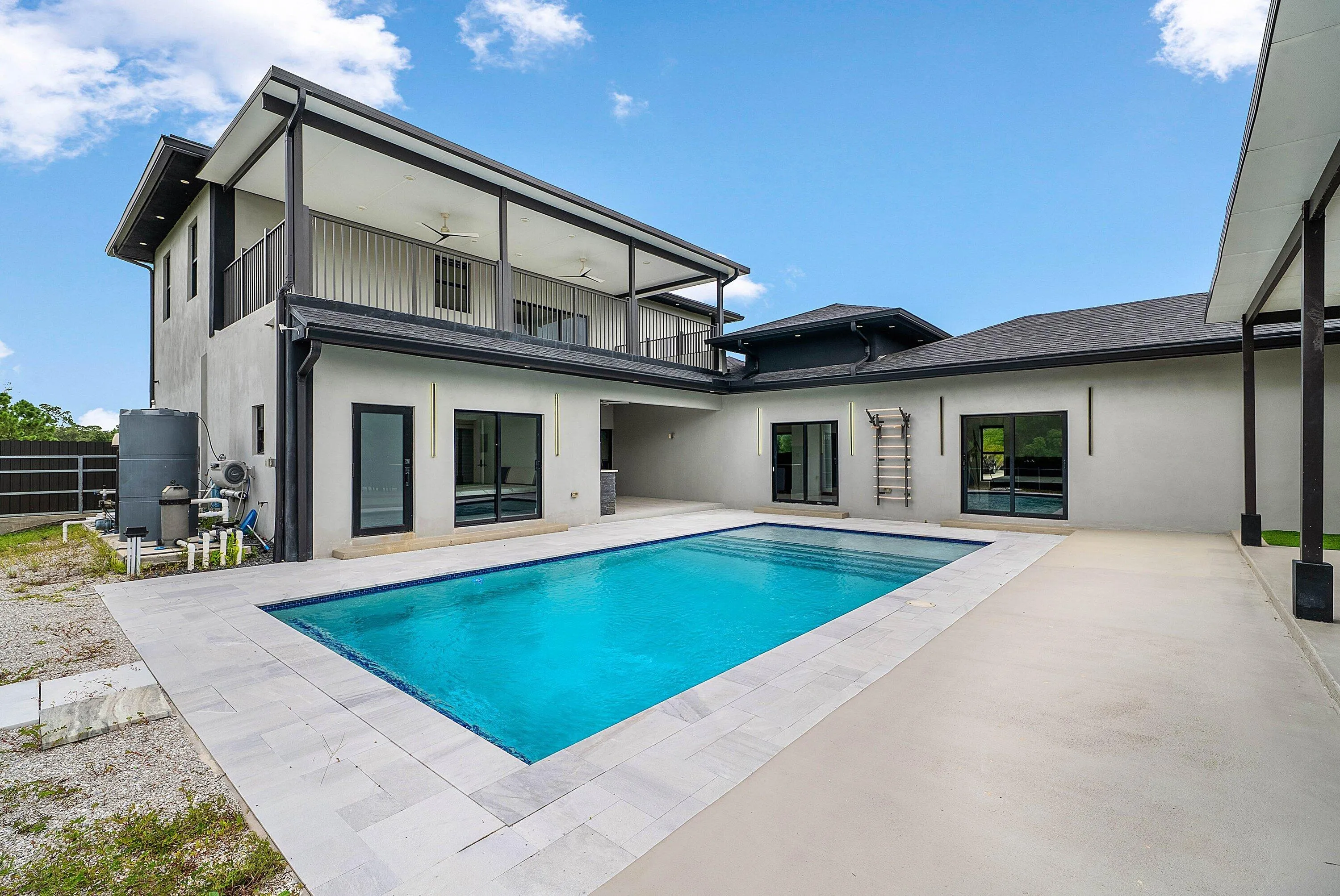 Rectangular swimming pool with tiled coping, surrounding concrete patio, and a two-story exterior featuring an upper-level balcony