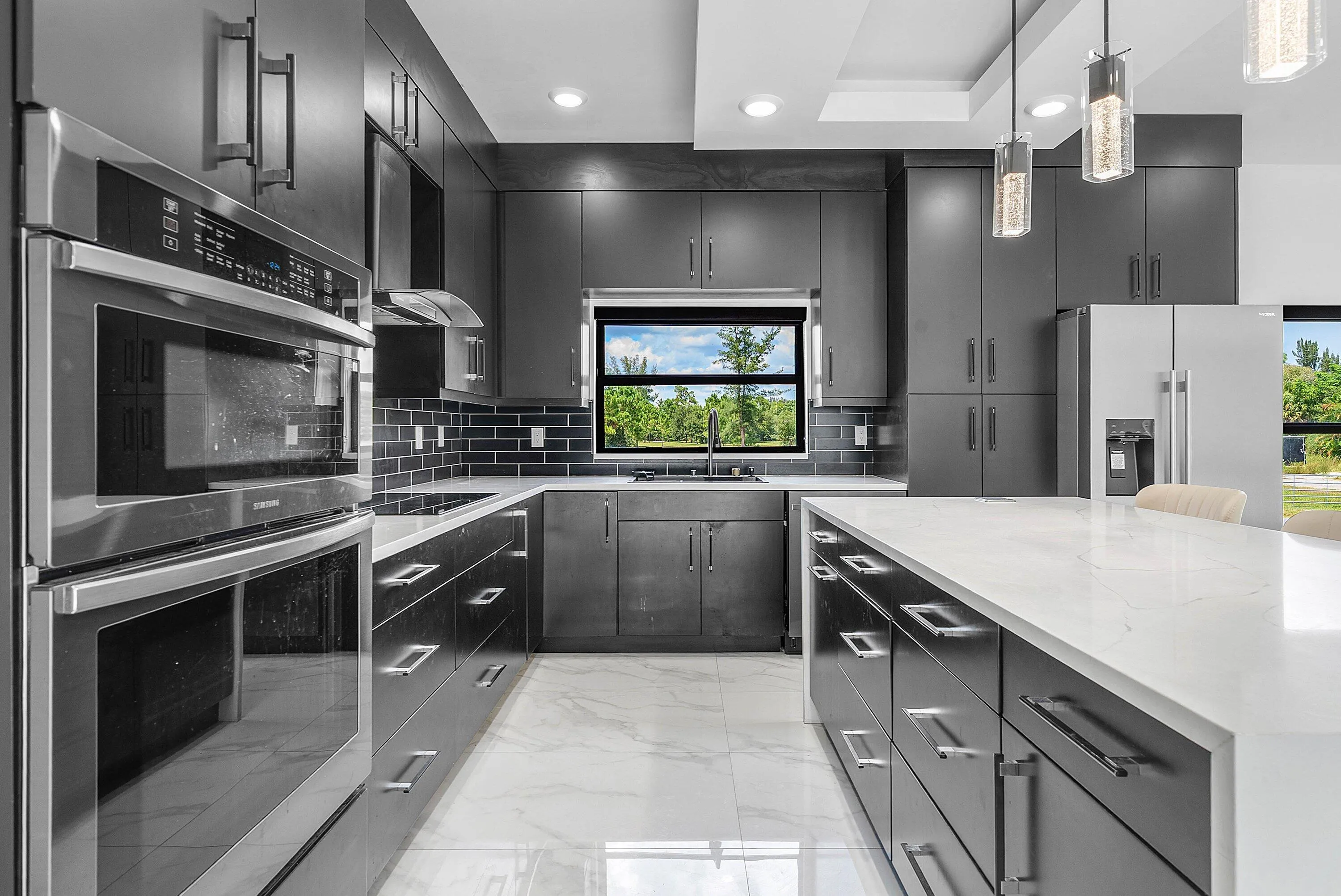 Kitchen with dark cabinetry, white countertops, built-in double oven, stainless steel appliances, and sleek pendant lighting