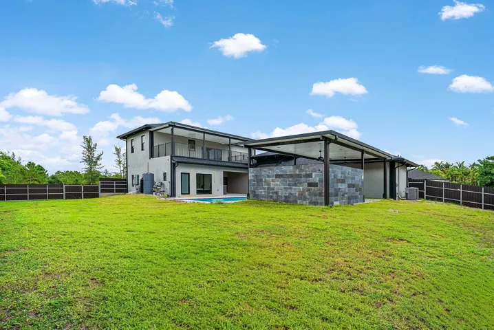 Expansive green lawn, two-story exterior, ground-level pool, upper-level balcony, and covered outdoor structure with stone-finish walls