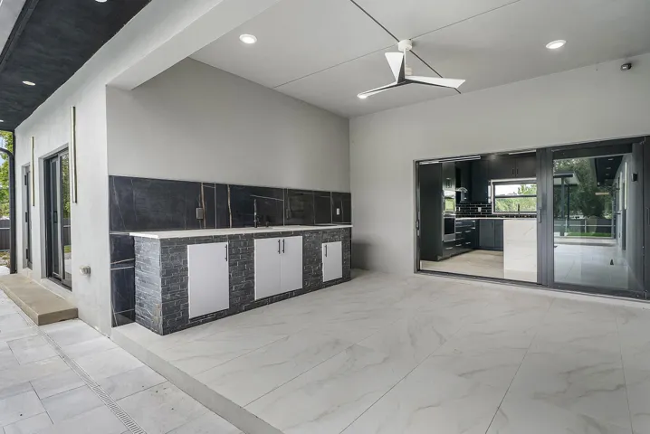 Covered outdoor living space featuring an integrated outdoor kitchen, contemporary ceiling fan, recessed lighting, and large format floor tiling