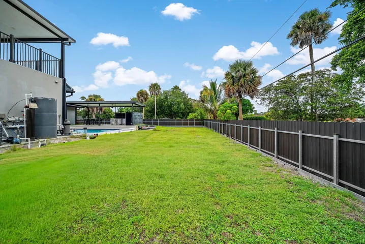 Expansive grass area with a dark panel fence, bordering a covered outdoor entertainment space and pool