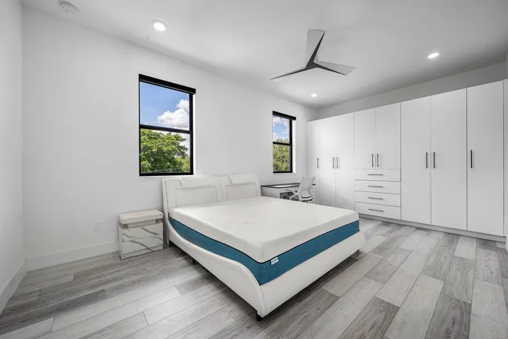 Expansive built-in wardrobe system with ample storage, contemporary ceiling fan, recessed lighting, wood-finish flooring, and multiple windows
