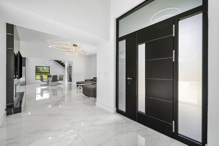 Modern entry door with frosted glass panels, white marble-look flooring, built-in media console, and a contemporary ceiling light fixture