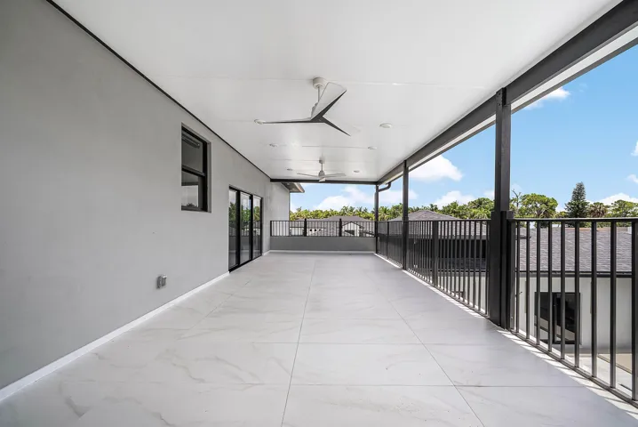 Expansive covered terrace with large format tile flooring, black metal railings, and dual ceiling fans