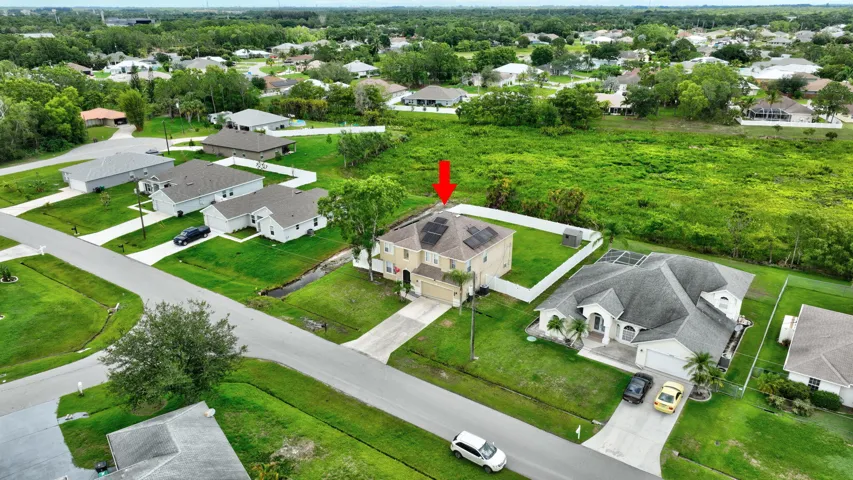 Two-story residence featuring a shingled roof, solar panels, a concrete driveway, and a white fence enclosing a portion of the property