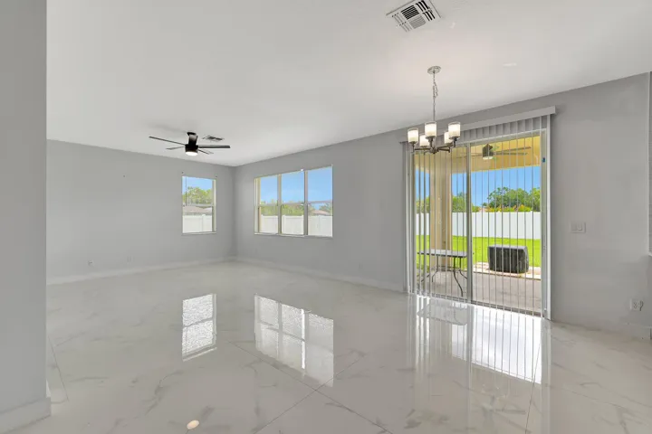 Expansive room featuring glossy tile flooring, multiple windows with blinds, a ceiling fan, a chandelier, and sliding glass doors to the exterior