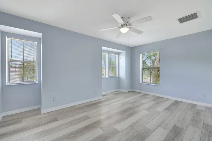 Spacious room featuring light wood-finish flooring, multiple windows, and a ceiling fan with integrated lighting
