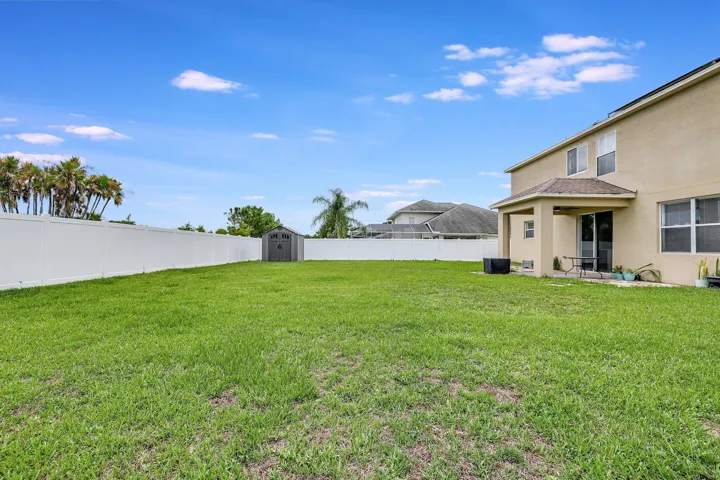 Expansive lawn with a white privacy fence, covered patio, and a storage shed