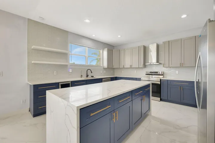 Kitchen featuring a large island with a waterfall countertop, two-tone cabinetry, stainless steel appliances, and a tiled backsplash