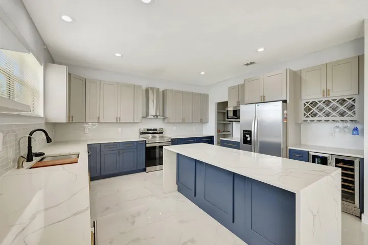 Kitchen featuring a large island with a waterfall countertop, two-tone cabinetry, stainless steel appliances, and a built-in wine rack with beverage cooler