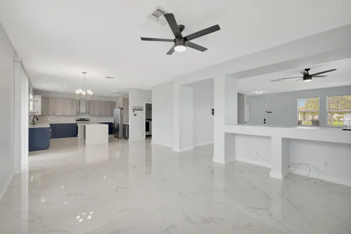 Open-concept living space featuring high ceilings, contemporary ceiling fans, polished tile flooring, and a kitchen with an island and built-in appliances