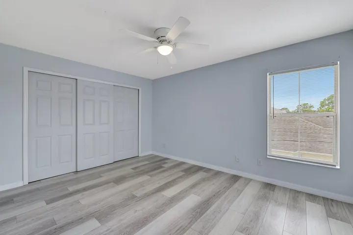 Wood-finish flooring, sliding panel closet doors, ceiling fan with integrated lighting, and a window with horizontal blinds
