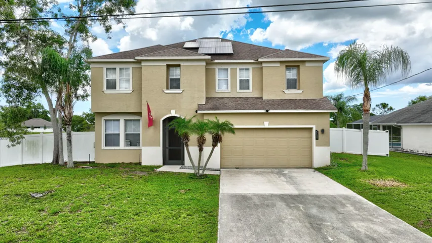 Two-story stucco exterior with an attached garage, paved driveway, and mature landscaping